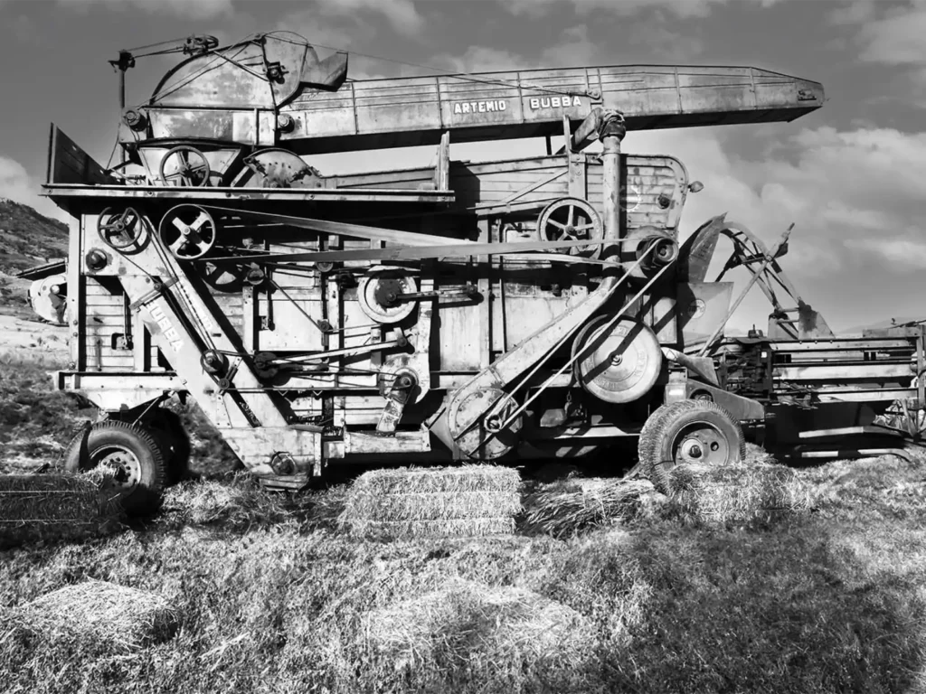 Vecchia trebbiatrice Artemio Bubba in un campo, tra balle di paglia, con le colline sullo sfondo, in bianco e nero