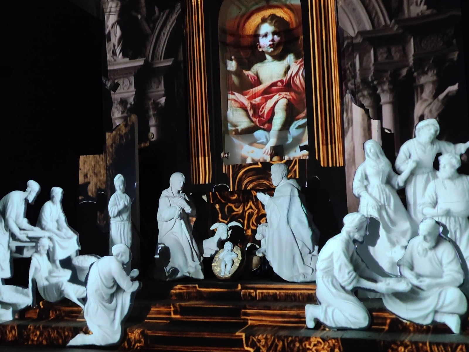 Statue bianche della Natività illuminate dal video mapping, con proiezioni di architetture barocche e del Bambino Gesù sullo sfondo