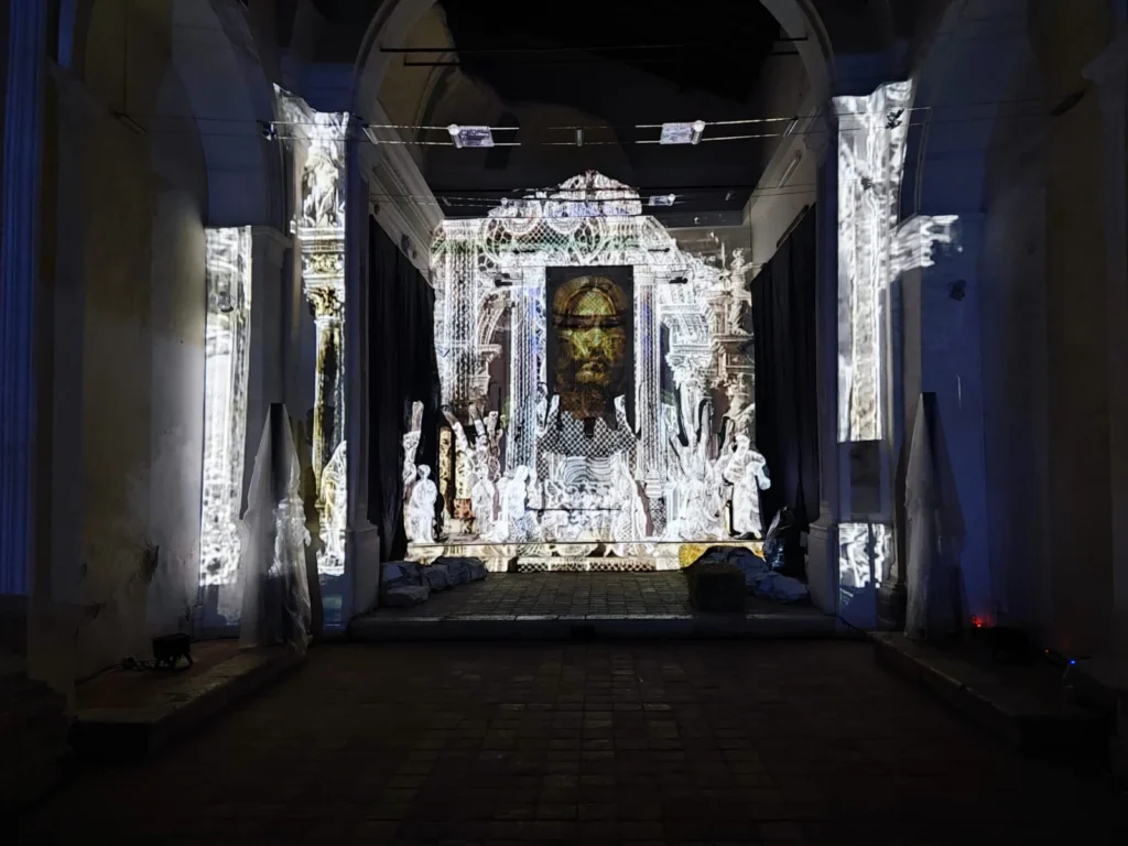 Navata della chiesa vista dall’ingresso, con architetture barocche e il volto di Cristo proiettati dal video mapping sulla scenografia del Presepe d’InCanto
